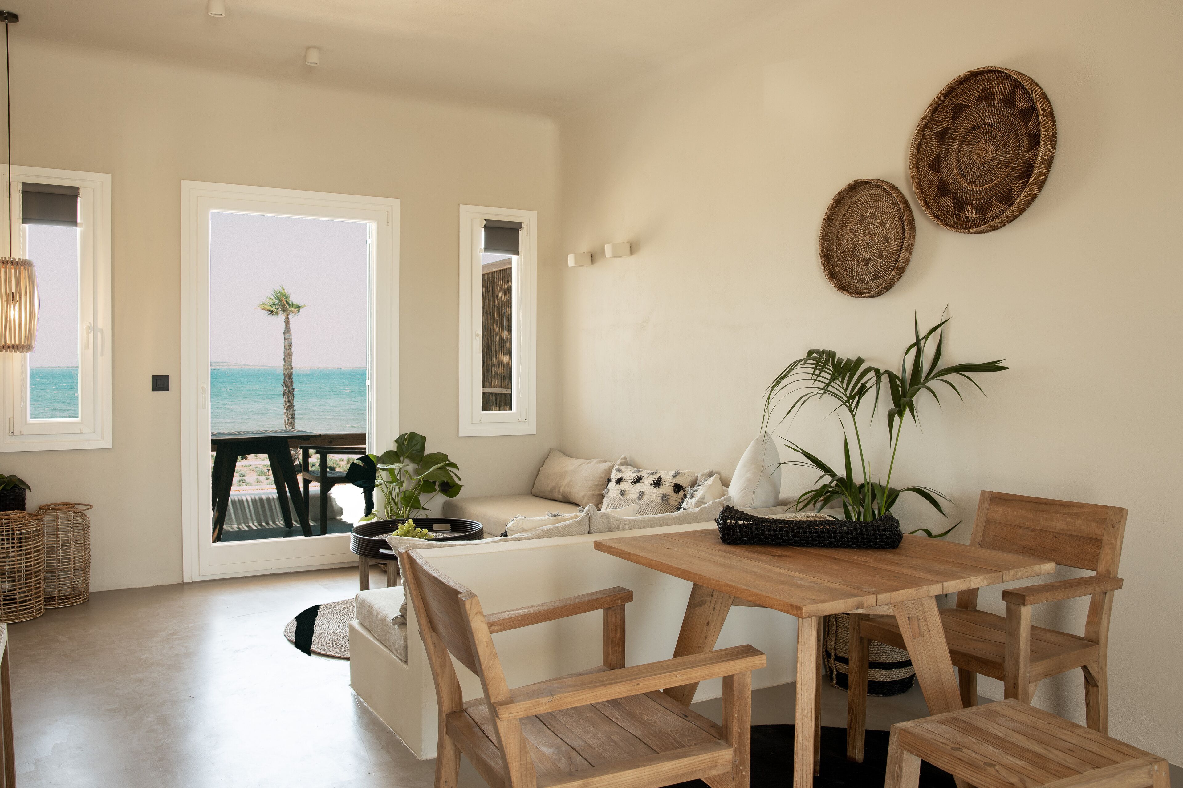 Amplia sala de estar con una mesa y sillas de madera, un sofá y vista al océano a través de grandes ventanales.