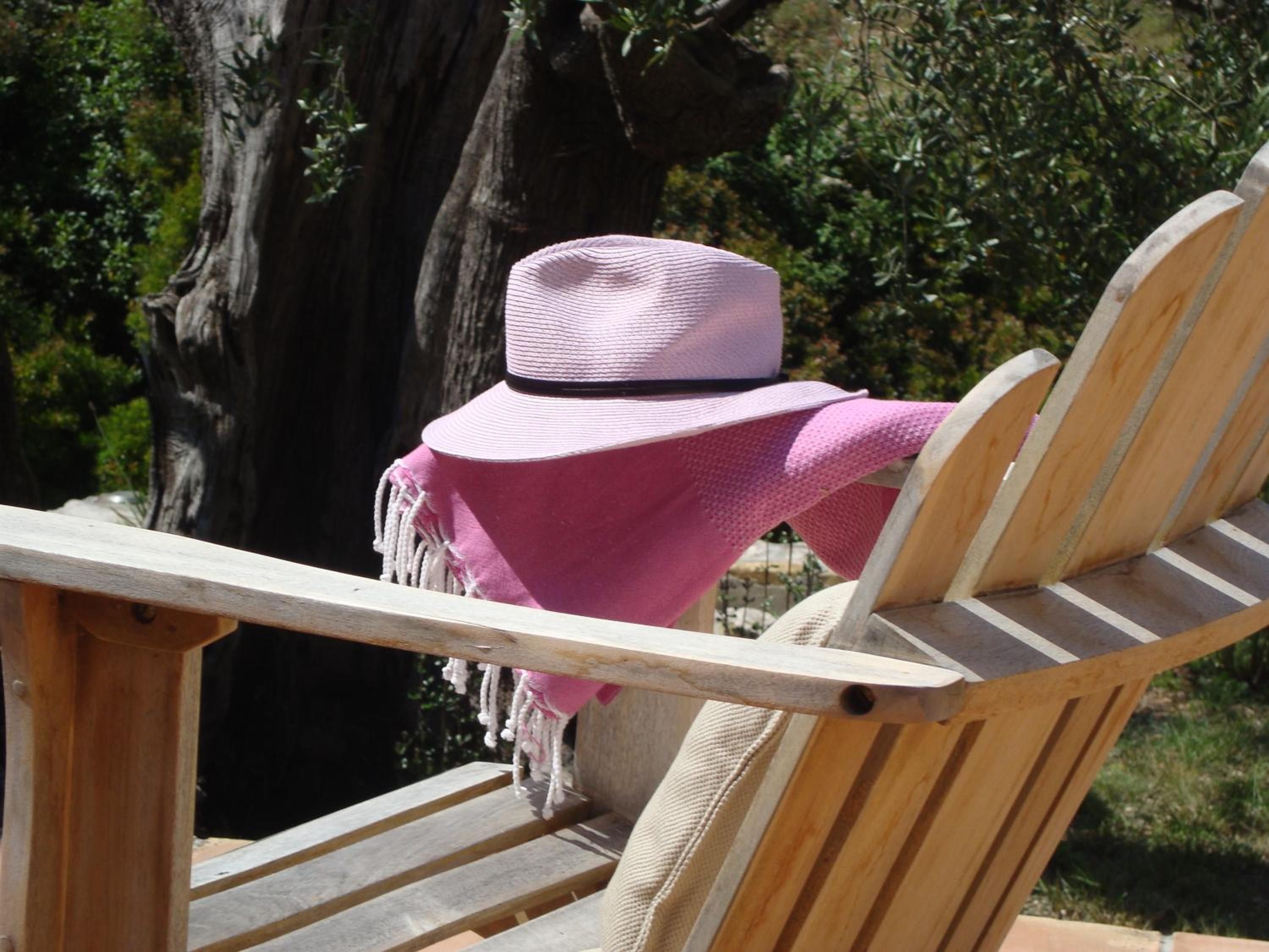 A wooden chair with a pink hat and a pink cloth draped over it.