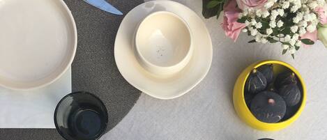 A table set with plates, bowls, spoons, a glass of water, a loaf of bread, a baguette, a croissant, and a yellow bowl with figs.