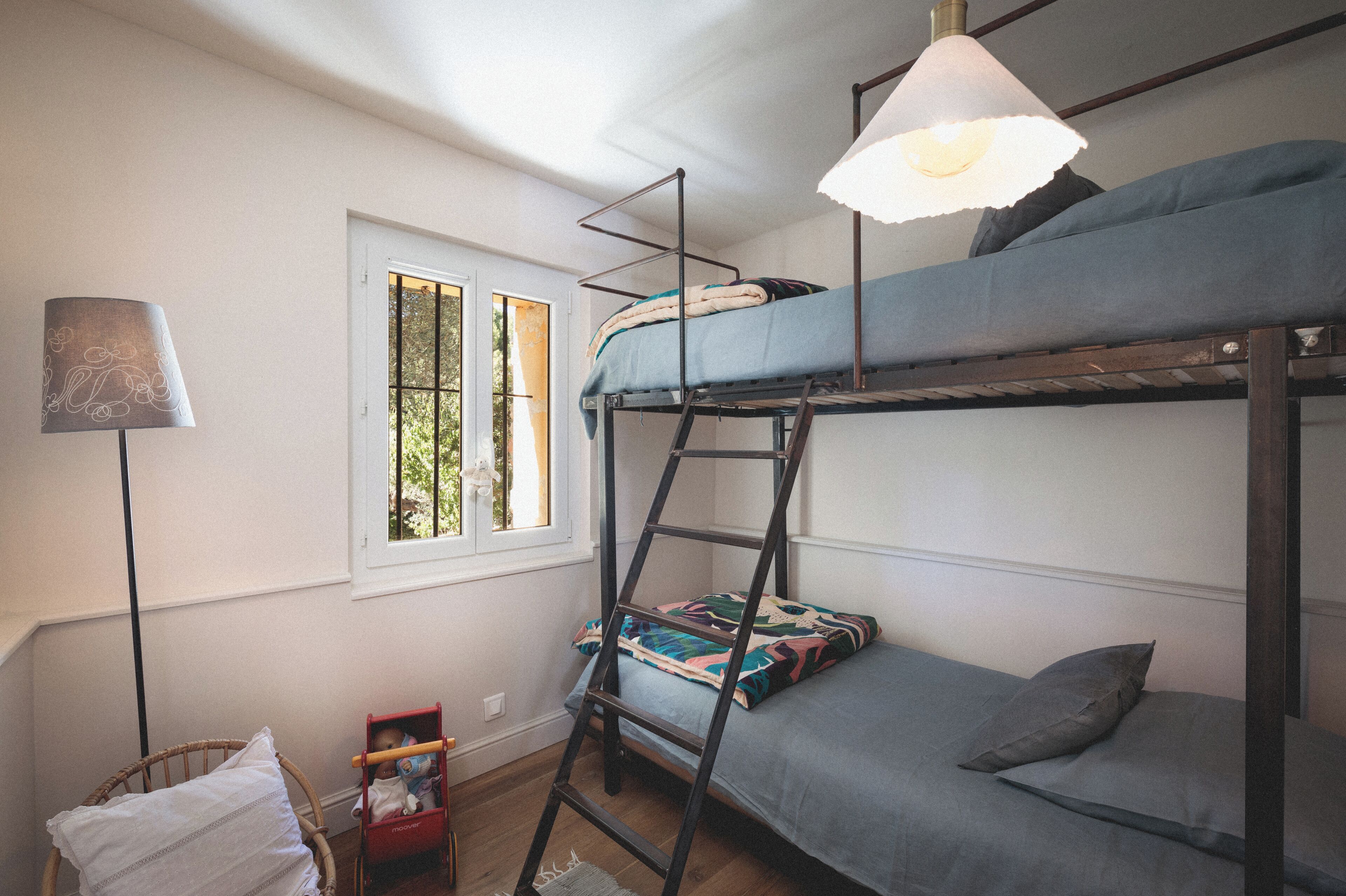 A bunk bed room with a ladder, a window, and a lamp.