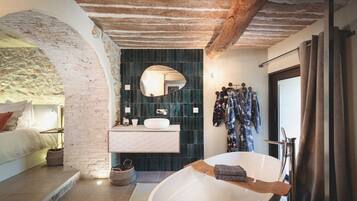 A modern bathroom with a freestanding bathtub, a large mirror, and a dark tiled wall.