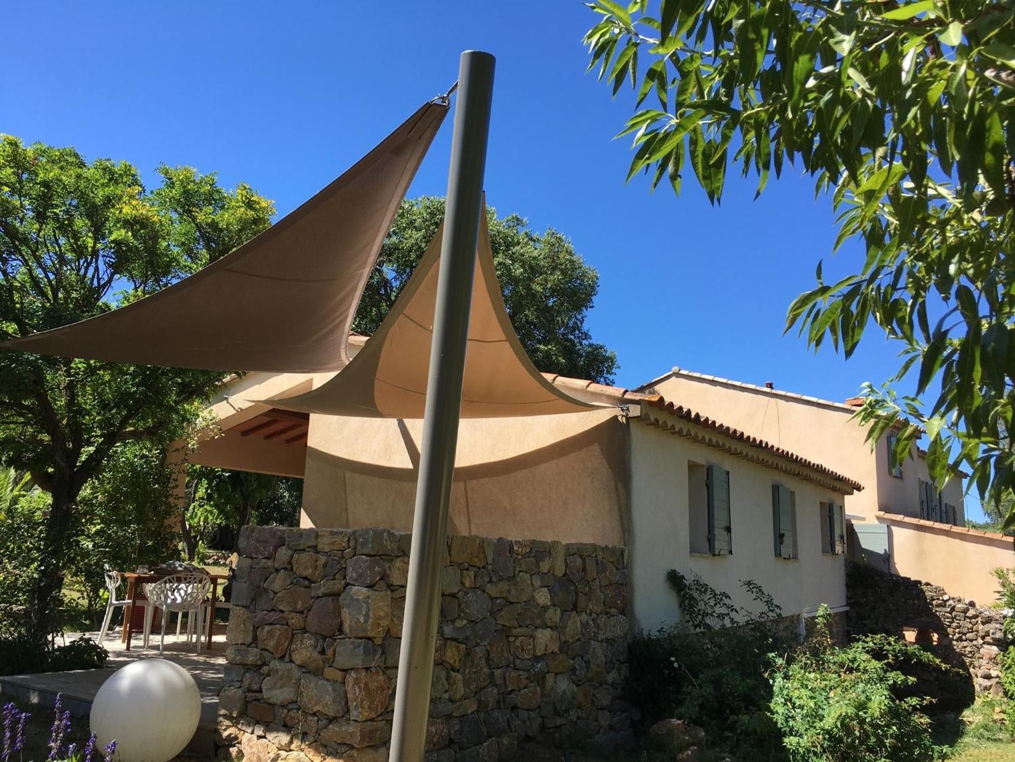 A building with a stone wall, a large shade sail, and a clear blue sky.