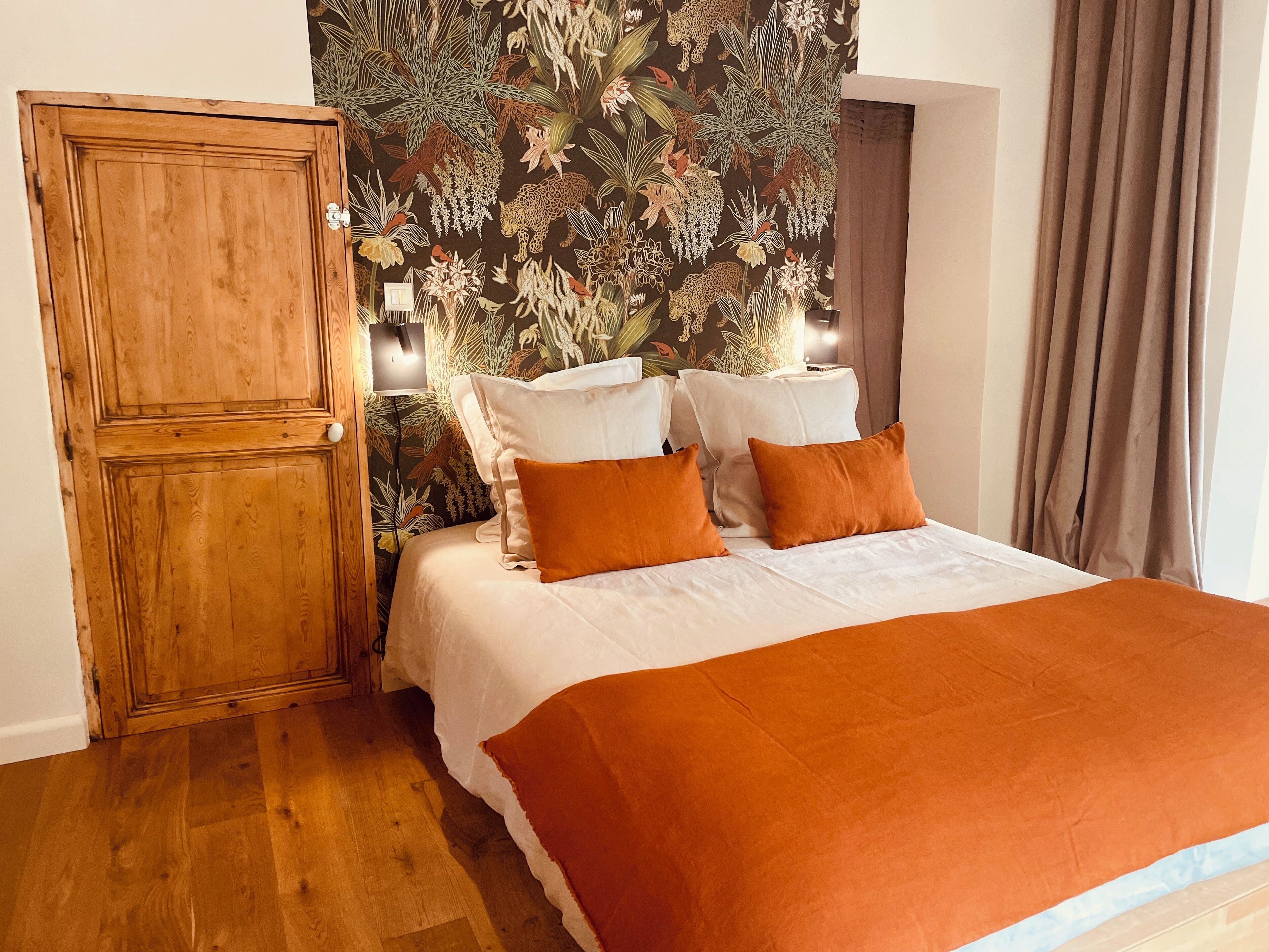 Un dormitorio con un armario de madera, una cama con ropa de cama blanca y naranja, y un papel tapiz floral.