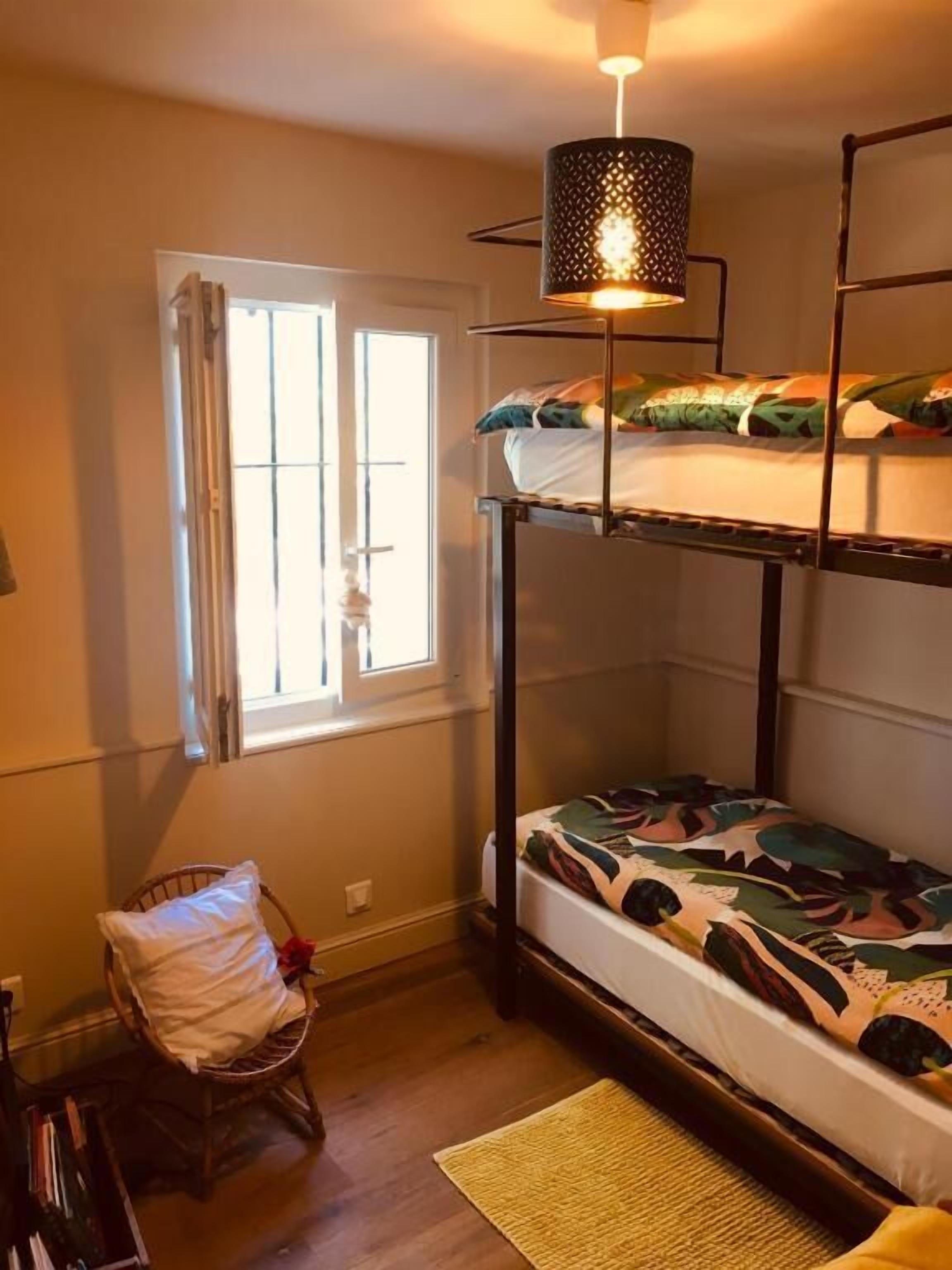 Ein Schlafraum mit Etagenbett, Fenster, Stuhl und Lampe.