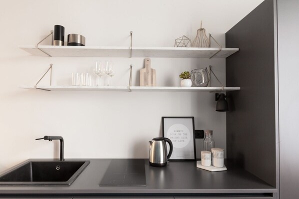 A modern kitchen with a black sink, stainless steel kettle, and white shelves holding various kitchen items.