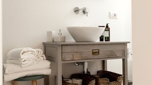 Une salle de bain avec un lavabo blanc, un miroir, un porte-serviettes et une petite table sur laquelle sont pliées des serviettes.