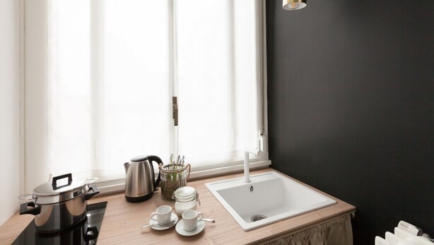 Une cuisine moderne avec un mur noir, un évier blanc et une fenêtre ornée de rideaux légers.