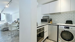 A modern kitchen with white cabinets, a microwave, a toaster, and a washing machine. - Tuynhuys (Cape Town)