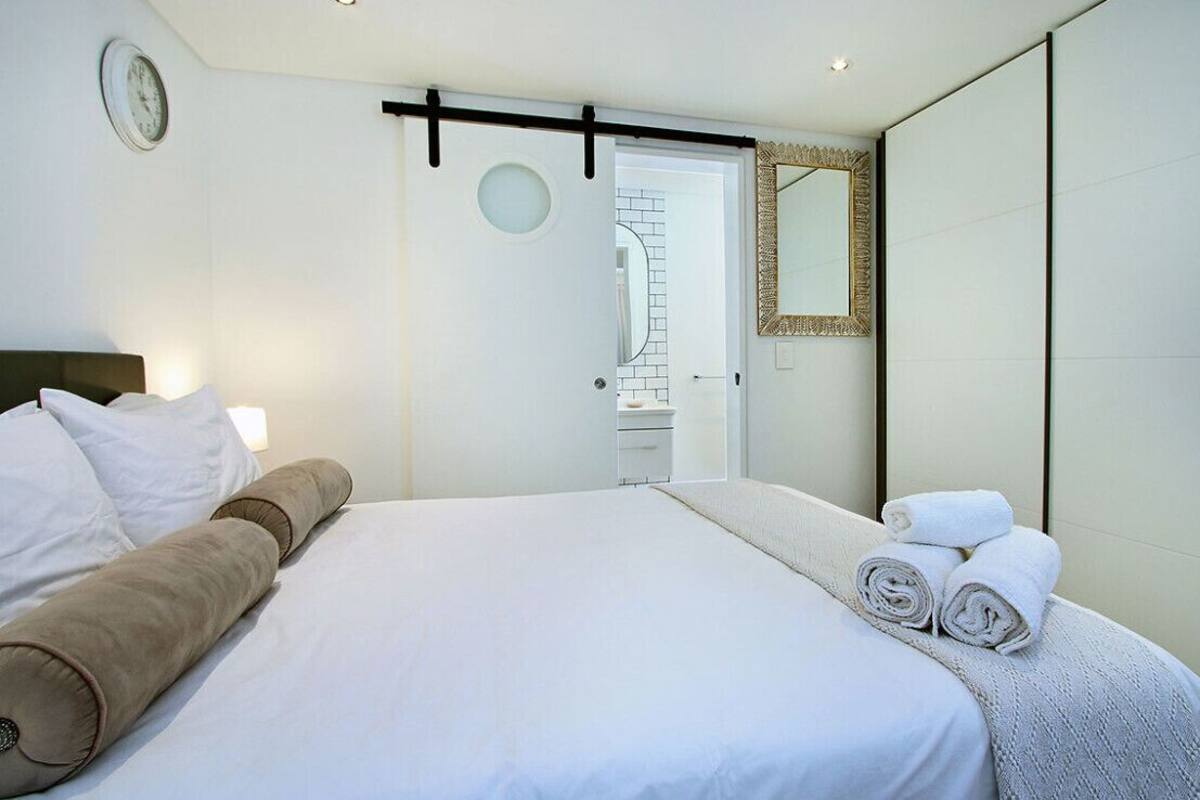 A modern hotel room with a large bed, a bedside table, a mirror, and a door leading to a bathroom.