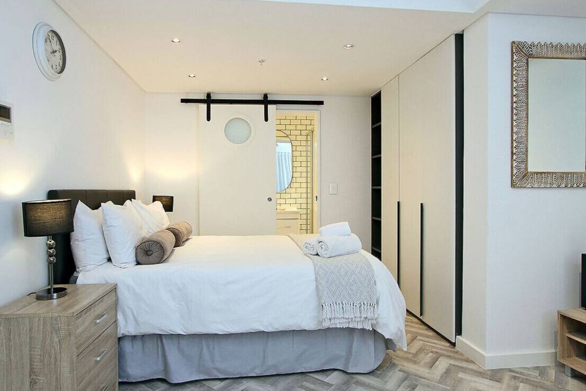 A modern bedroom with a bed, bedside table, and a mirror.