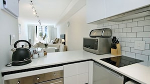 A modern kitchen with white cabinetry, a built-in microwave, and a kettle. - Tuynhuys (Cape Town)