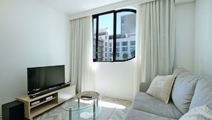 A modern living room with a flat-screen TV on a wooden stand, a glass coffee table, and a grey sofa. - Tuynhuys (Cape Town)
