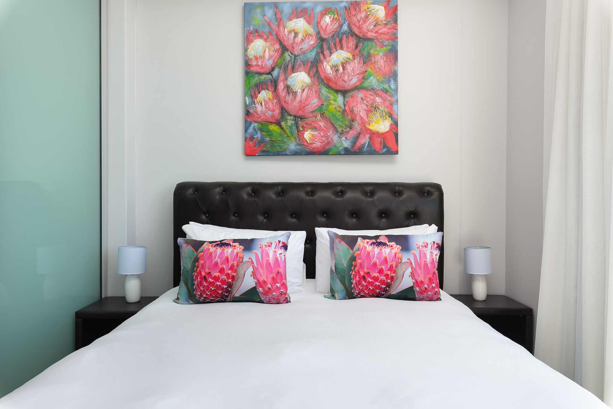 A hotel room with a bed, two nightstands, a tufted headboard, and a painting above the bed.