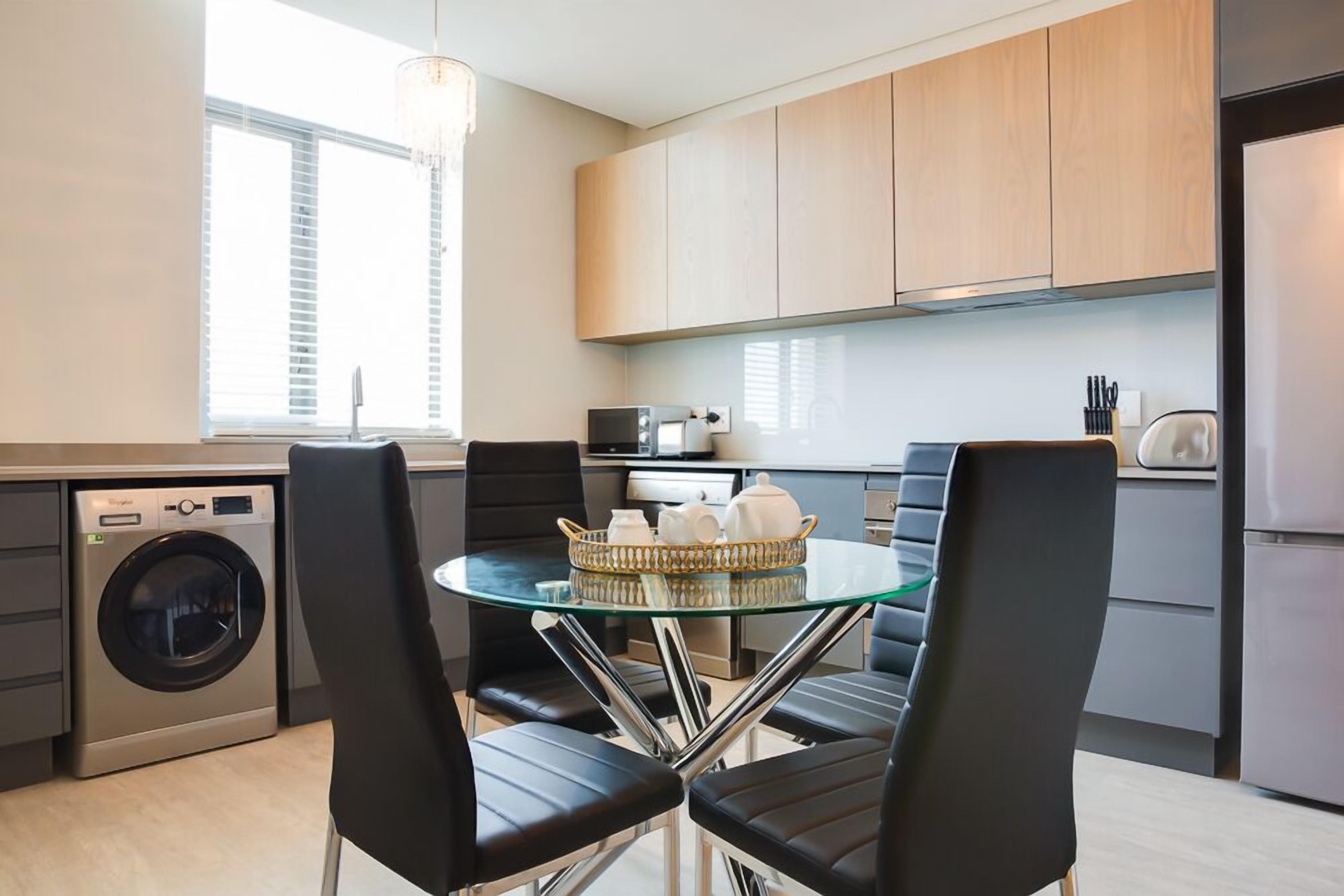 Une cuisine compacte équipée d’un lave-linge, d’une table à manger avec des chaises et de meubles de rangement en bois.