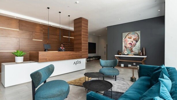 Un área de recepción moderna con un mostrador de madera, sillas tapizadas en azul y un sofá color aguamarina.