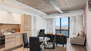 A modern living room with a sofa, chairs, a dining table, and a kitchen area with cabinets and a kettle. - Matrix (Cape Town)