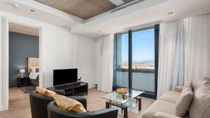 A modern living room with a flat-screen TV, two sofas, a glass coffee table, and a large window offering a view of the city. - Matrix (Cape Town)