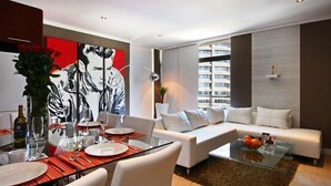 Una sala de estar moderna con una mesa de comedor de vidrio, sofás blancos y un cuadro abstracto grande.