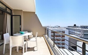 Varanda com mesa e cadeiras, vista para edifícios e guarda-corpo.