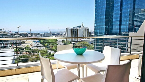 Ein Balkon mit rundem Tisch und Stühlen, einer dekorativen Schale und Blick auf die Stadt.