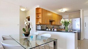 Eine moderne Küche mit Holzschränken, einem Glastisch und weißen Stühlen.