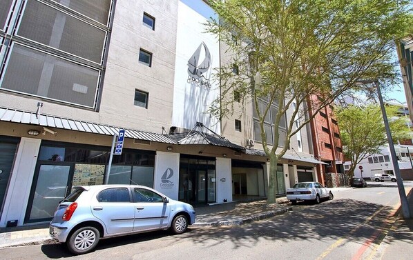 Um edifício com um grande logotipo de veleiro, um carro prateado estacionado e uma rua arborizada.