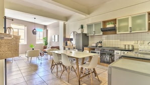 A modern kitchen with a dining area, featuring a large island, white cabinetry, and a tiled floor. - The Piazza (Cape Town)