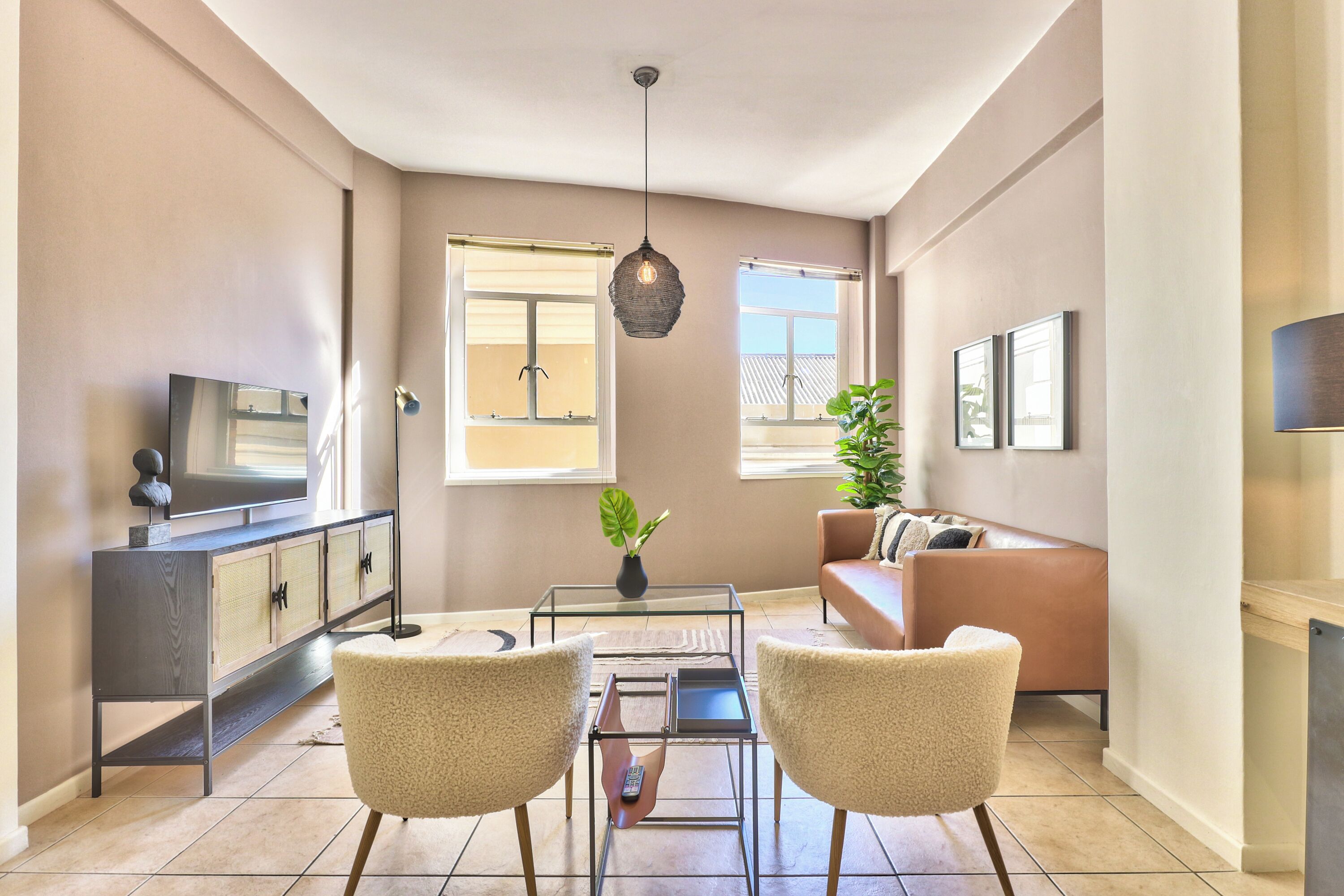 Una sala de estar moderna con un sofá, dos sillones, una mesa de centro, un televisor y una planta.
