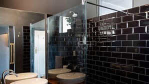 Ein modernes Badezimmer mit zwei Waschbecken, einer Duschkabine aus Glas und schwarzen Fliesenwänden.