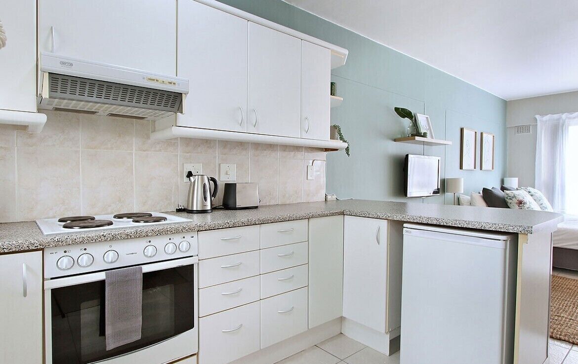 A compact kitchen with white cabinets, a built-in stove, and a small refrigerator.
