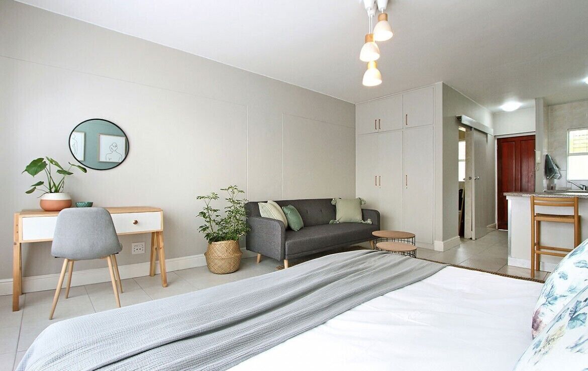 Ein modernes Schlafzimmer mit einem Bett, einem Schreibtisch, einem Stuhl, einer Couch und einer Topfpflanze.