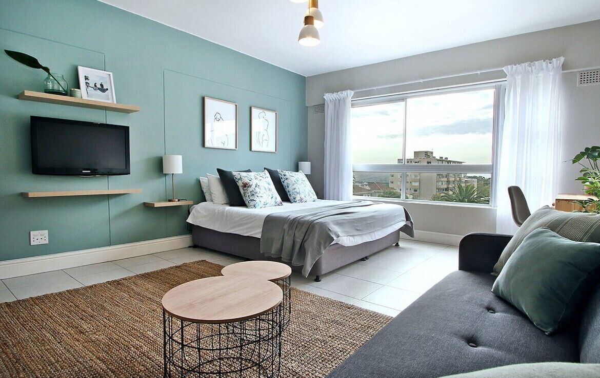 A modern bedroom with a bed, a TV, a sofa, and a window with a city view.