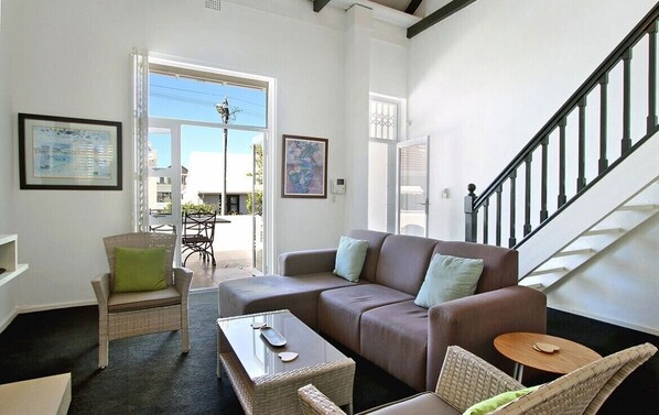 A modern living room with a brown sofa, wicker chairs, and a glass coffee table. A staircase is visible to the right.