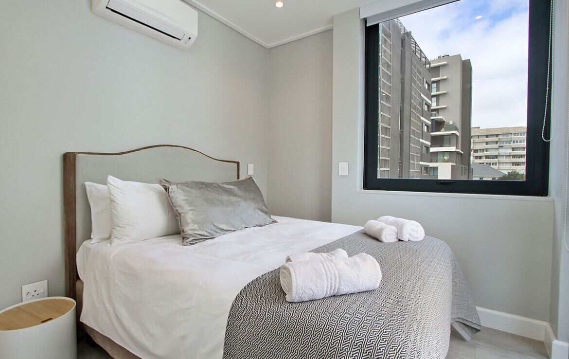 Ein modernes Hotelzimmer mit einem Bett, einem Fenster mit Blick auf die Stadt und einem kleinen Nachttisch.