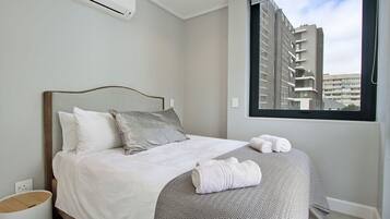 A modern hotel room with a bed, a window with a city view, and a small bedside table.
