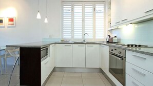 A modern kitchen with white cabinets, a granite countertop, a built-in oven, and a window with blinds.