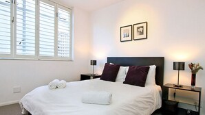 A neatly made bed with white linens and two rolled towels, a dark headboard, and two bedside lamps on nightstands.
