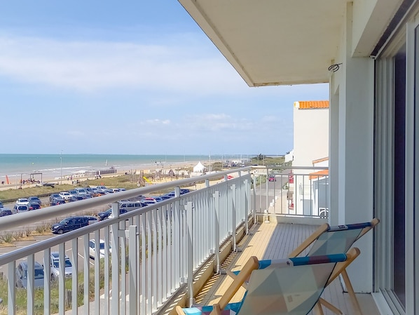 Een balkon met uitzicht op het strand en geparkeerde auto's.