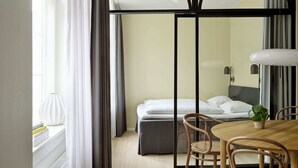 Una stanza con un letto, un tavolo da pranzo con sedie, una pianta in vaso e una finestra con tende.