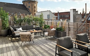 A shared rooftop terrace with outdoor seating, potted plants, and a view of the cityscape.