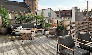 Eine Dachterrasse mit einer Couch, StĂŒhlen, einem Tisch und Topfpflanzen.