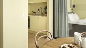 Een compacte hotelkamer met een kitchenette, een eethoek met tafel en stoelen, en een bed met uitzicht.