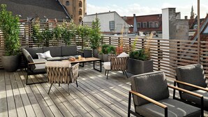 En fælles tagterrasse med udendørs møbler, plantekasser og udsigt over bybilledet.