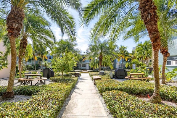 A pathway flanked by palm trees and benches, leading to a building with a covered patio area.