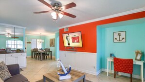 A living room with a ceiling fan, a dining area with a table and chairs, and a kitchen with cabinets and a window.