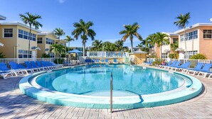 A circular pool with blue lounge chairs and palm trees, surrounded by buildings with balconies.