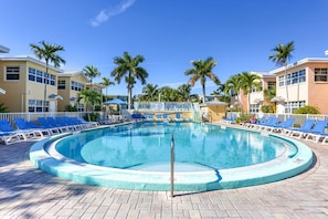 A circular pool with blue lounge chairs around it, palm trees, and a clear sky.