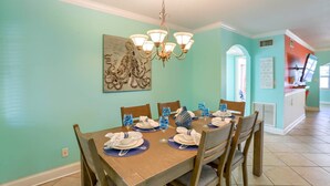 A dining area with a wooden table set for six, a chandelier, and a teal-colored wall with a painting.