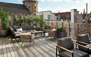 Una terraza compartida en la azotea con mobiliario exterior, plantas en macetas y vistas panorámicas de la ciudad.