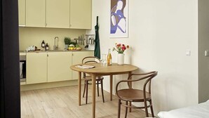 Quarto compacto com mesa de jantar de madeira, duas cadeiras, cama e uma cozinha compacta com armários e pia.